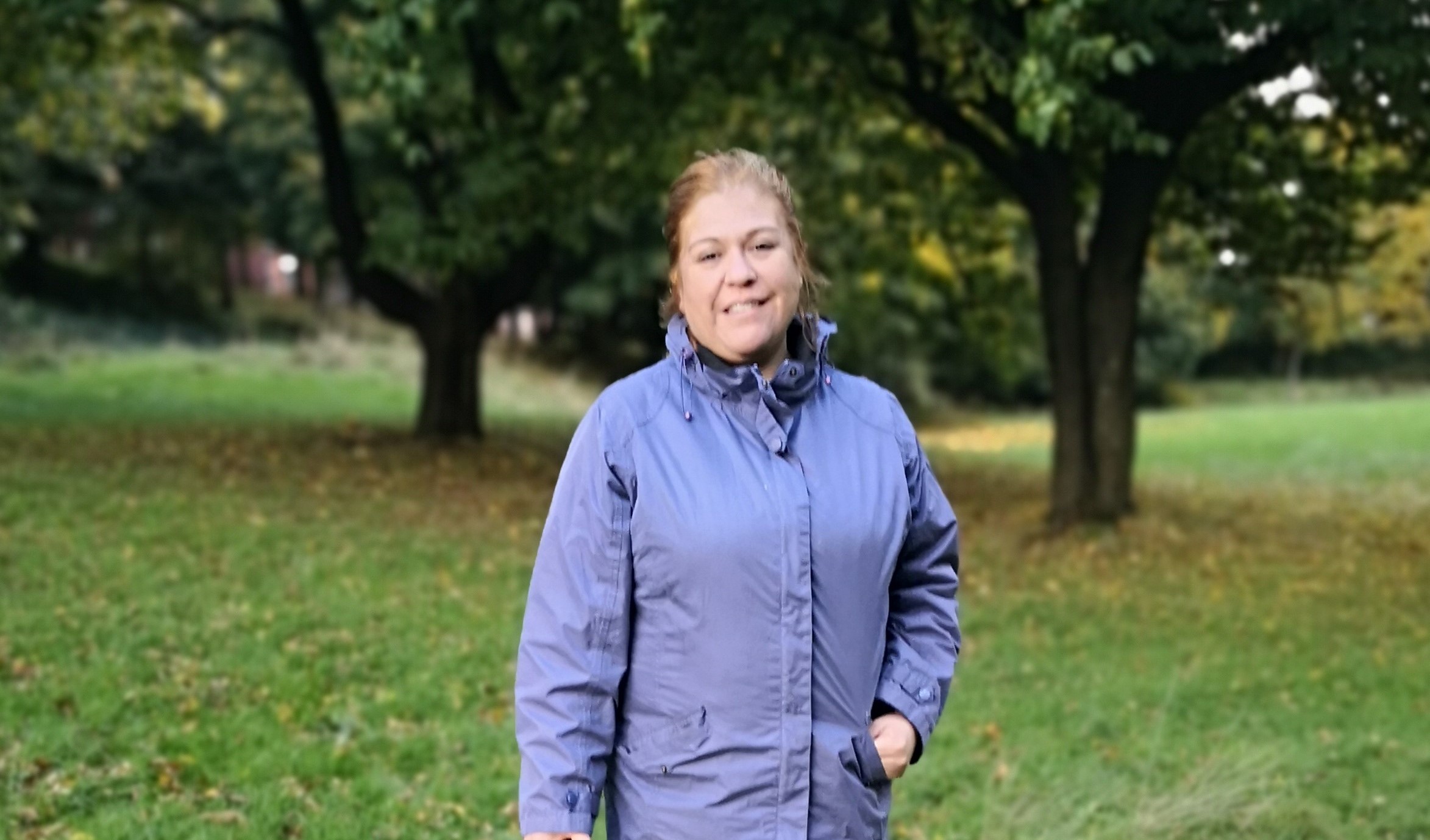 Lady standing in front of trees smiling wearing a purple coat