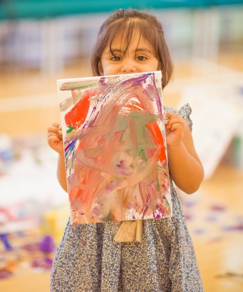 This image shows a little girl holding up a painted canvas she has created