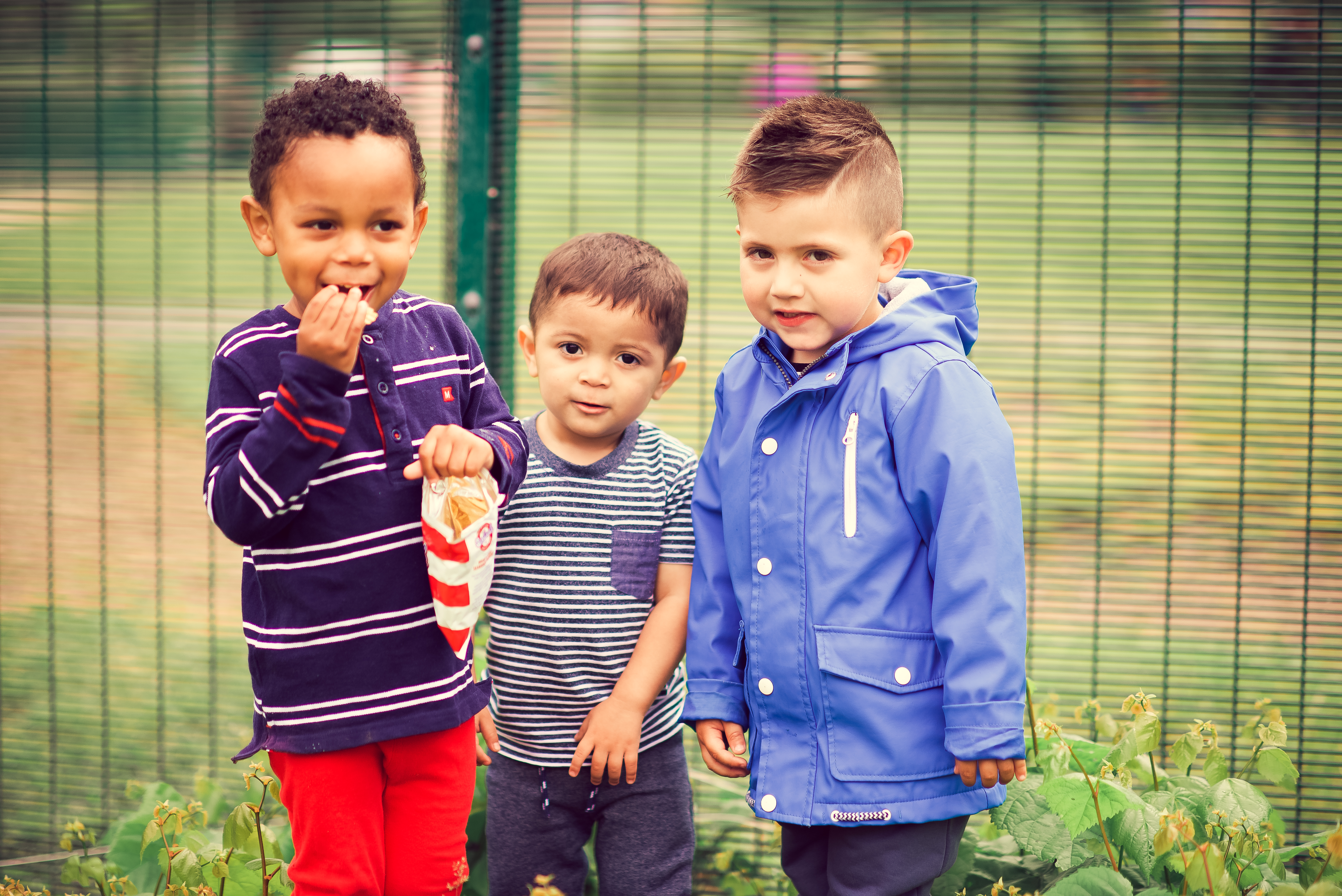 This image shows three young people stood in front of a fence with a field behind them they are all smiling