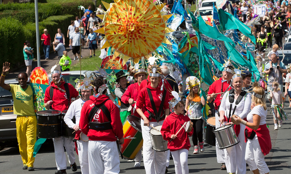 This image is from Darnhill festival its of the Darnhill parade everyone is happy and smiling holding decorated pieces of art